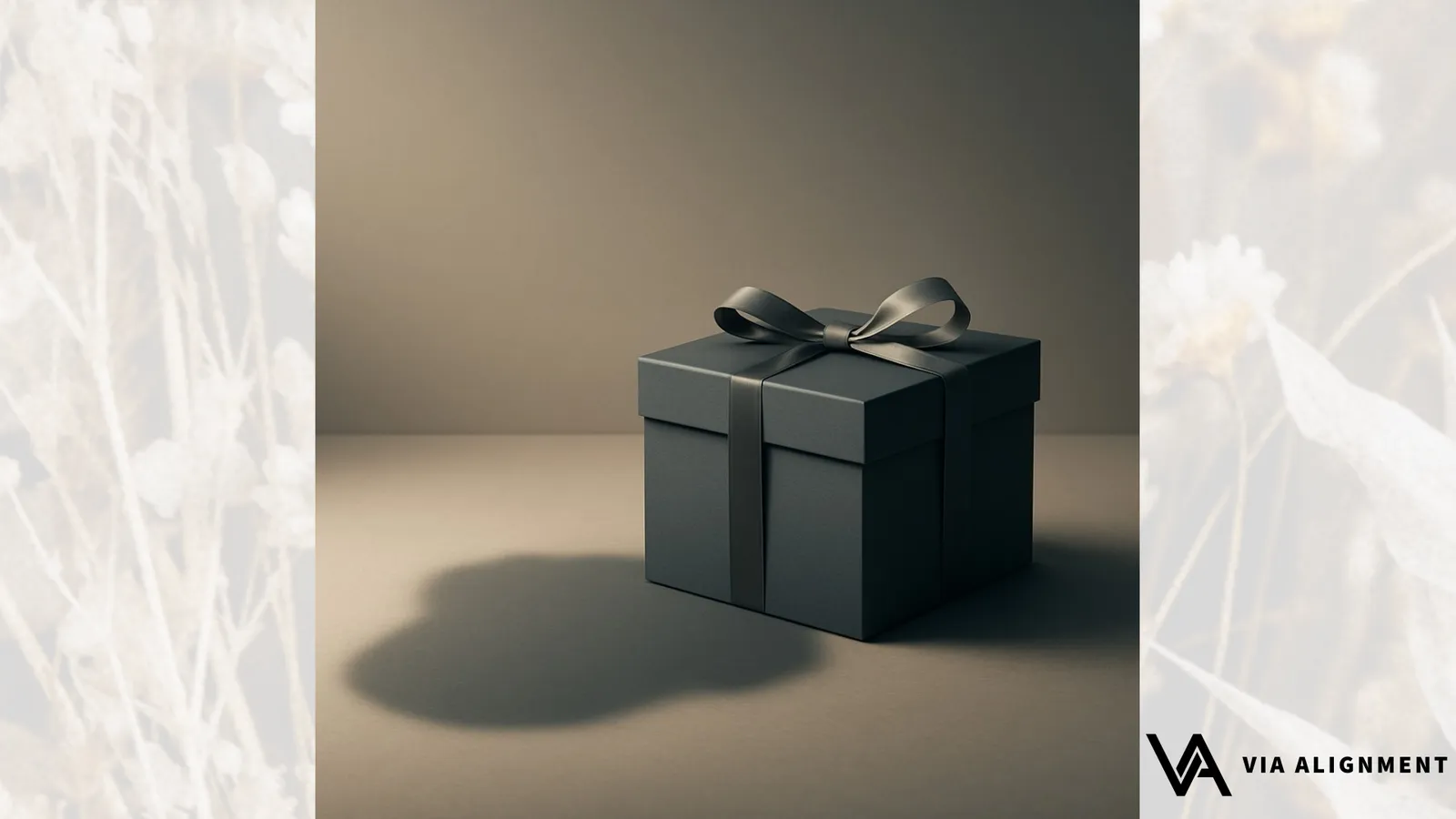 A dark gift box tied with a satin ribbon bow, sitting on a plain surface with a soft shadow.